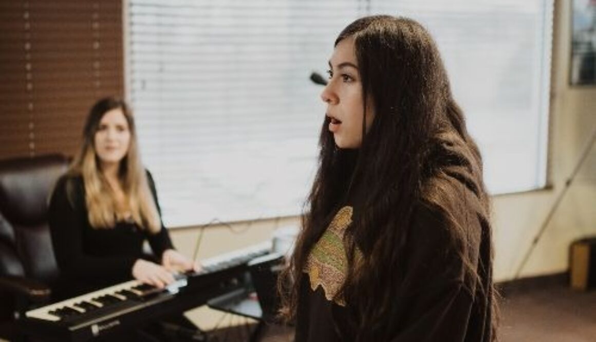 A young girl singing during her vocal lesson with her teacher playing piano