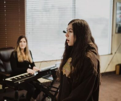 A young girl singing during her vocal lesson with her teacher playing piano